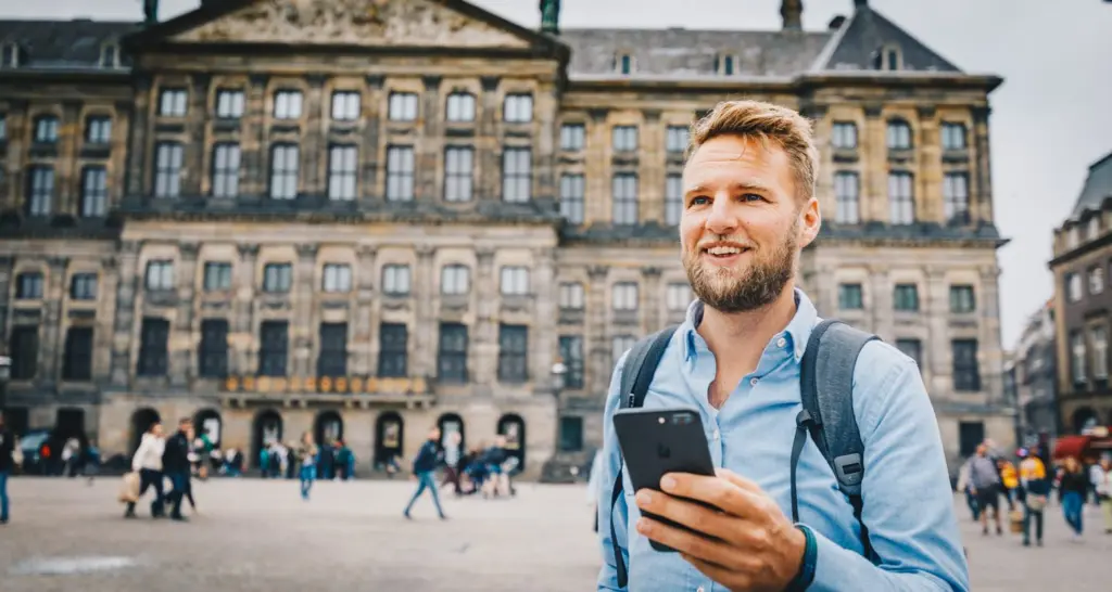 Ein Mann steht auf einem Stadtplatz und nutzt Voys VoIP auf seinem Handy mit einer österreichischen 0720-Nummer ohne geografische Bindung.