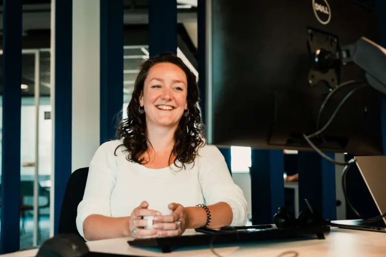 Een foto van een lachende collega van Voys die naar een computerscherm kijkt met een kop koffie in de hand